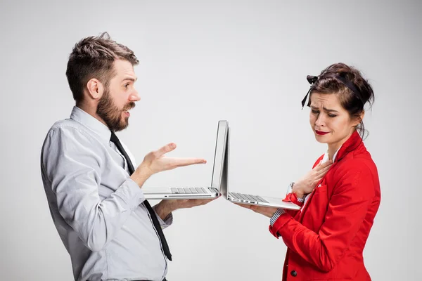 El joven hombre de negocios y mujer de negocios con ordenadores portátiles que se comunican sobre fondo gris — Foto de Stock