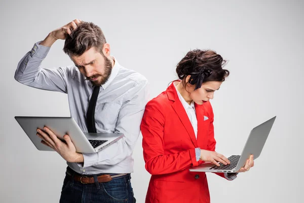 El joven hombre de negocios y mujer de negocios con ordenadores portátiles que se comunican sobre fondo gris — Foto de Stock