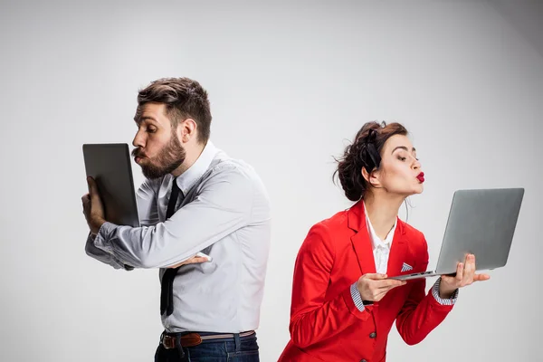 Il giovane uomo d'affari e donna d'affari con computer portatili che baciano schermi su sfondo grigio — Foto Stock
