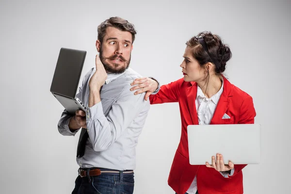 De jonge zakenman en zakenvrouw met laptops communiceren op grijze achtergrond — Stockfoto