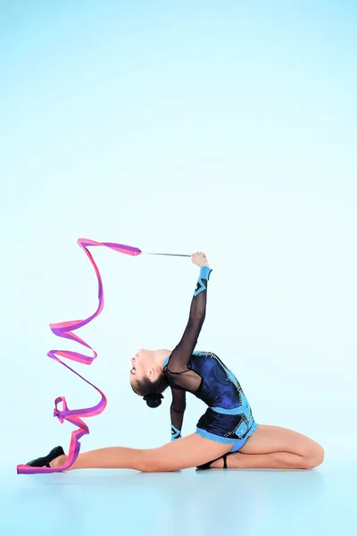 Het meisje doet Turnen dans met gekleurd lint op een blauwe achtergrond — Stockfoto