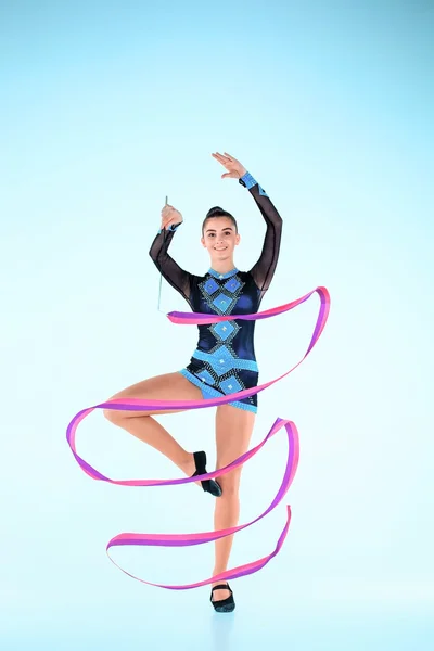 La chica que hace gimnasia baila con cinta de colores sobre un fondo azul —  Fotos de Stock