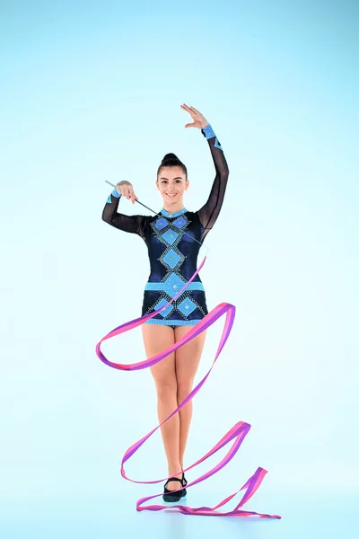 Девушка танцует гимнастику с цветной лентой на синем фоне — стоковое фото