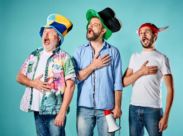 Die drei Fußballfans singen die Nationalhymne über blau — Stockfoto