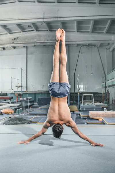 Caucásico hombre gimnasia acrobacias equilibrio postura en gimnasio fondo — Foto de Stock