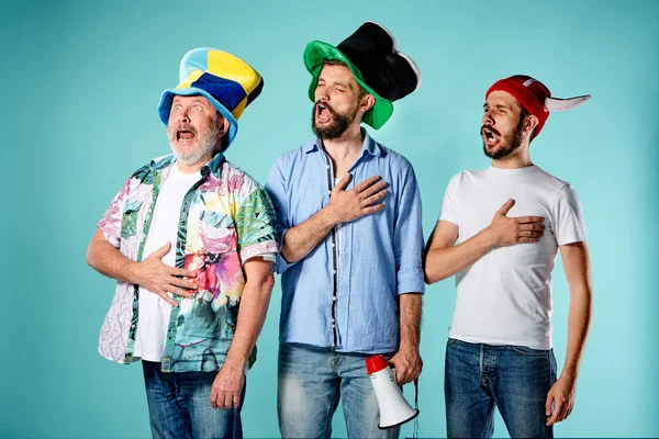 Os três fãs de futebol cantando o hino nacional sobre azul — Fotografia de Stock