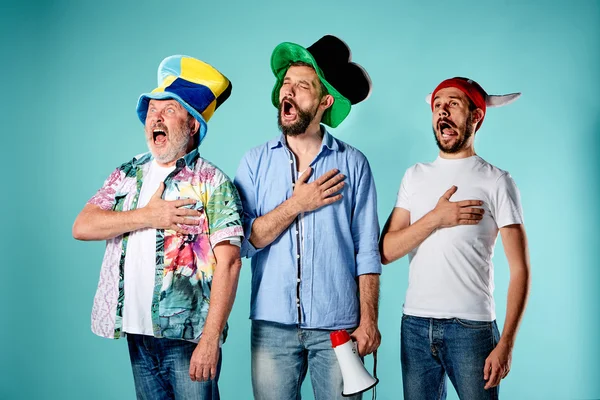 De drie voetbalfans het volkslied zingen over blauw — Stockfoto