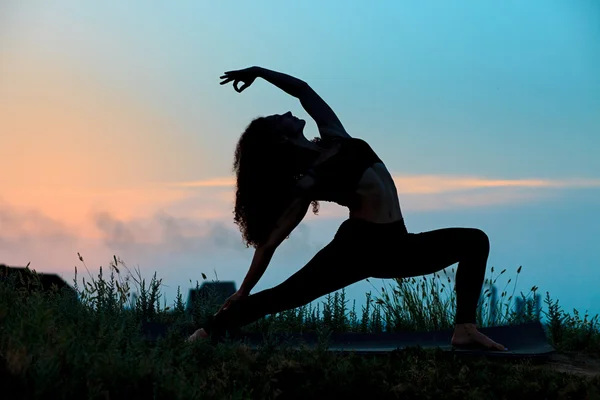 Силуэт молодой женщины практикует йогу — стоковое фото