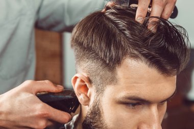 The hands of young barber making haircut to attractive man in barbershop clipart