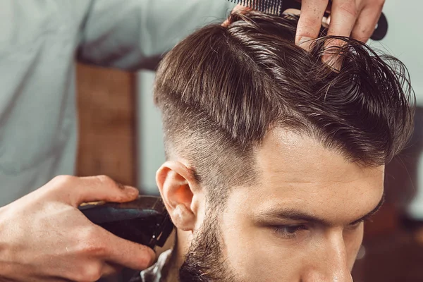 The hands of young barber making haircut to attractive man in barbershop Royalty Free Stock Photos