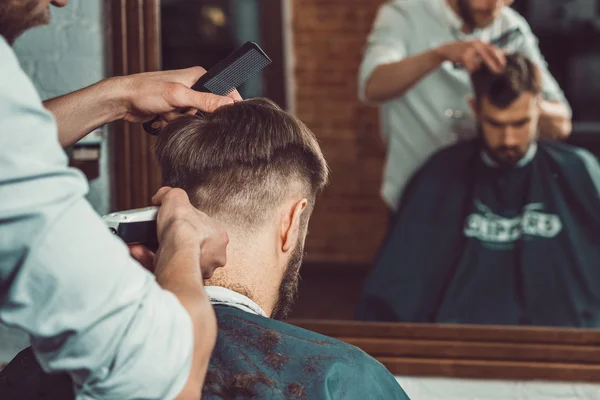 Die Hände eines jungen Friseurs, der einem attraktiven Mann im Friseursalon die Haare schneidet — Stockfoto