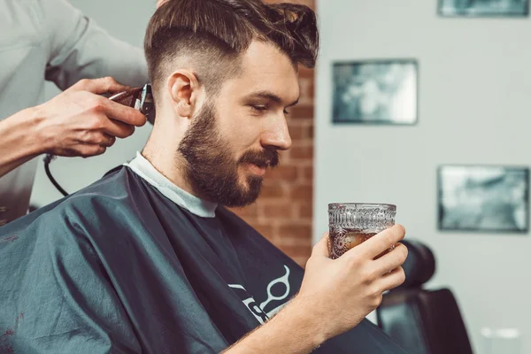 Le mani del giovane barbiere fare taglio di capelli a uomo attraente in barbiere — Foto Stock