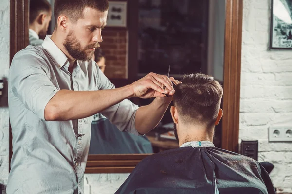 Giovane bel barbiere che fa taglio di capelli di uomo attraente in barbiere — Foto Stock