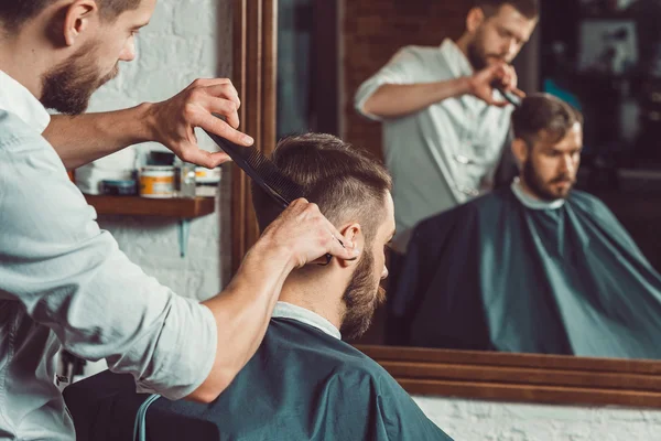 Jeune beau coiffeur faisant coupe de cheveux de l'homme attrayant dans le salon de coiffure — Photo