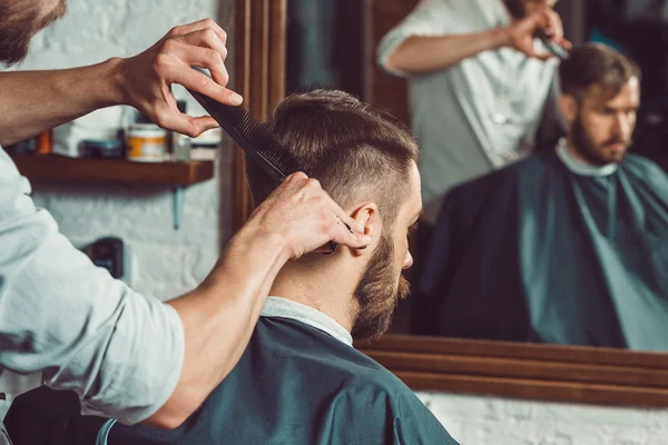 Las manos del joven peluquero haciendo corte de pelo a un hombre atractivo en la barbería — Foto de Stock