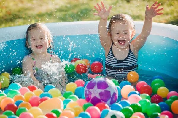 De to små babyjentene leker med leker i oppblåsbart basseng om sommeren, solskinnsdag – stockfoto
