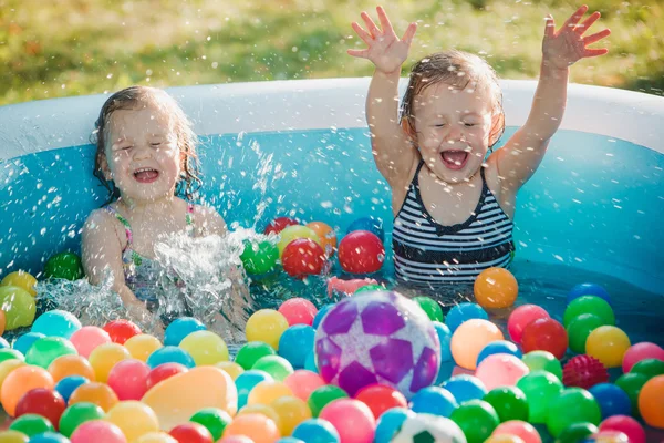 Les deux petites filles de bébé jouant avec des jouets dans la piscine gonflable dans la journée ensoleillée d'été — Photo