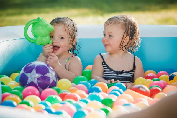 Les deux petites filles de bébé jouant avec des jouets dans la piscine gonflable dans la journée ensoleillée d'été — Photo