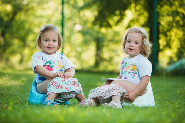 緑の草に対してトイレに座っている2人の小さな女の子 — ストック写真