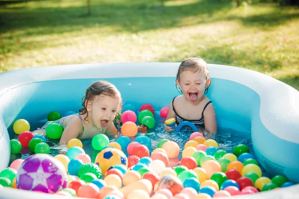 Οι δύο μικρό μωρό κορίτσια που παίζουν με τα παιχνίδια στη φουσκωτή πισίνα στην ηλιόλουστη μέρα το καλοκαίρι — Φωτογραφία Αρχείου