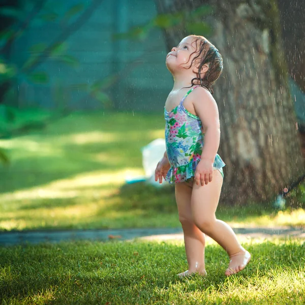 A pequena menina brincando com aspersor de jardim . — Fotografia de Stock