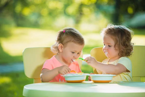 Két kislány ül az asztalnál, és együtt eszik ellen zöld gyep — Stock Fotó