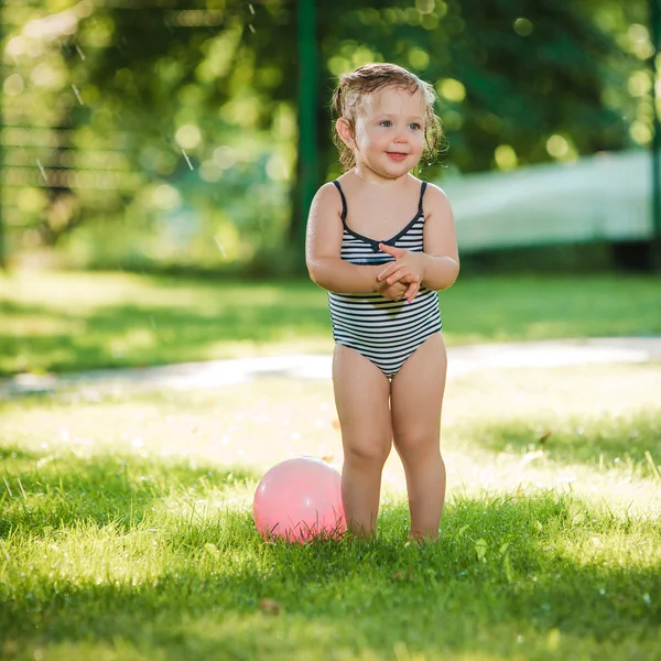A pequena menina brincando com aspersor de jardim . — Fotografia de Stock