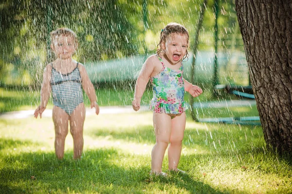 Las dos niñas jugando con aspersor de jardín . — Foto de Stock