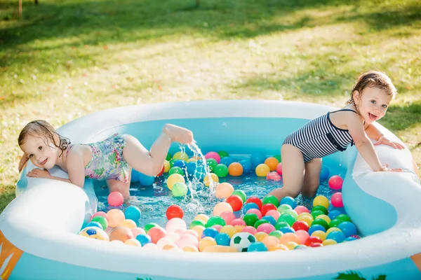 Las dos niñas jugando con juguetes en la piscina inflable en el día soleado del verano —  Fotos de Stock