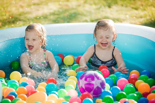 Las dos niñas jugando con juguetes en la piscina inflable en el día soleado del verano — Foto de Stock