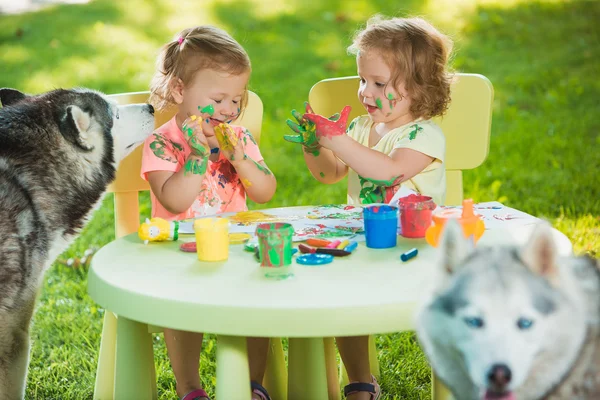 Two-year old girls painting with poster paintings together against green lawn — Stock Photo, Image