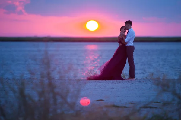 Fiatal szerelmespár pihentető a strandon, a naplementében — Stock Fotó