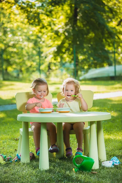 Dos niñas sentadas en una mesa y comiendo juntas contra el césped verde — Foto de Stock