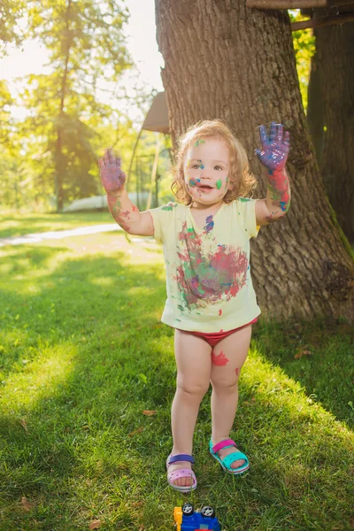 Menina de dois anos manchada em cores contra gramado verde — Fotografia de Stock