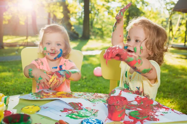 Two-year old girls painting with poster paintings together against green lawn — Stock Photo, Image