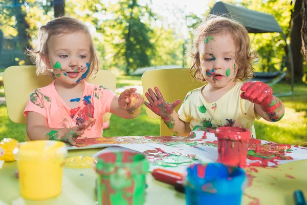 Two-year old girls painting with poster paintings together against green lawn — Stock Photo, Image