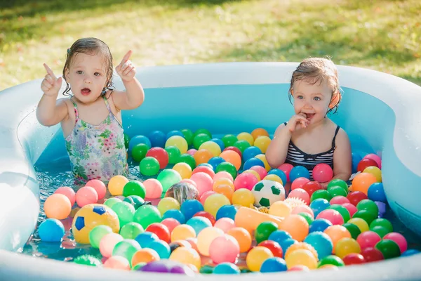 Las dos niñas jugando con juguetes en la piscina inflable en el día soleado del verano —  Fotos de Stock