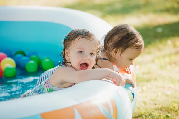 Las dos niñas jugando con juguetes en la piscina inflable en el día soleado del verano — Foto de Stock