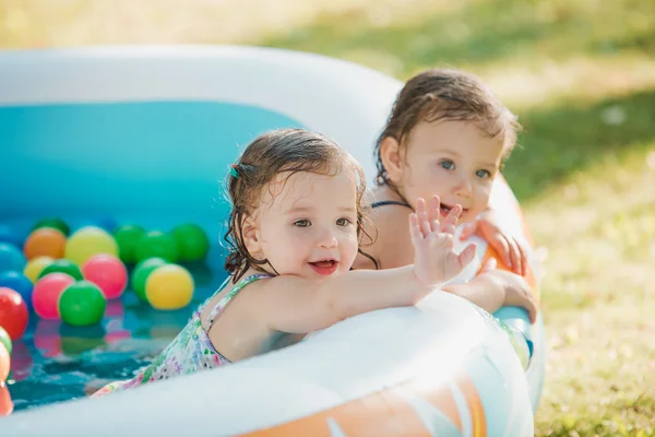 Οι δύο μικρό μωρό κορίτσια που παίζουν με τα παιχνίδια στη φουσκωτή πισίνα στην ηλιόλουστη μέρα το καλοκαίρι — Φωτογραφία Αρχείου