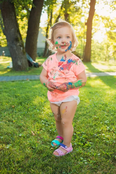 Niña de dos años manchada de colores contra césped verde — Foto de Stock