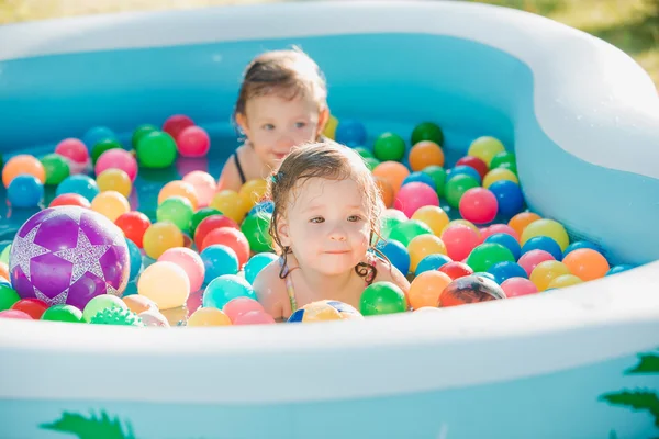 Les deux petites filles de bébé jouant avec des jouets dans la piscine gonflable dans la journée ensoleillée d'été — Photo