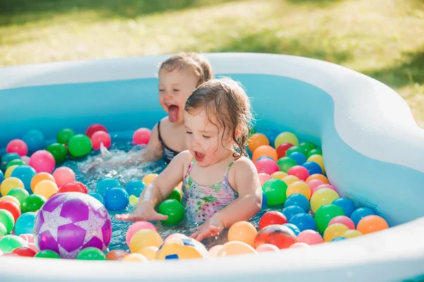 Las dos niñas jugando con juguetes en la piscina inflable en el día soleado del verano — Foto de Stock