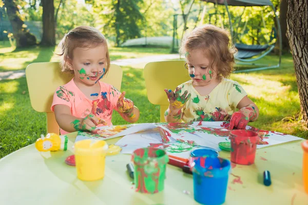 Two-year old girls painting with poster paintings together against green lawn — Stock Photo, Image