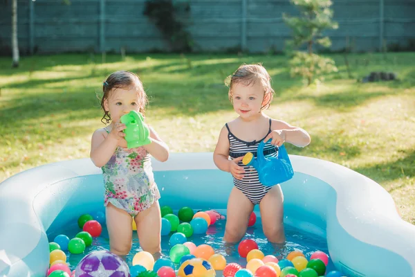 Две маленькие девочки играют с игрушками в надувном бассейне в летний солнечный день — стоковое фото