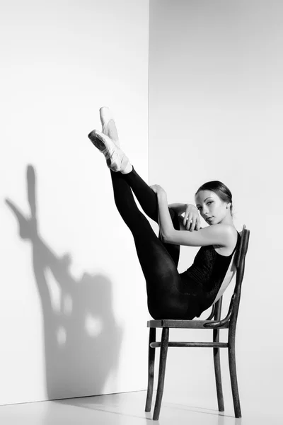 Балерина в черном наряде позирует на деревянном стуле, на фоне студии . — стоковое фото