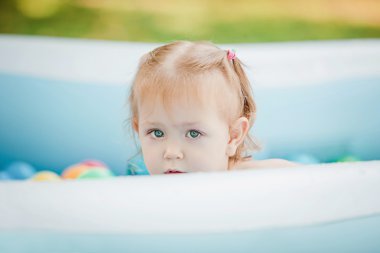 Yaz güneşli bir günde şişme havuz oyuncakları ile oynarken küçük bebek kız
