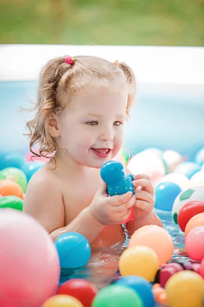 Το μικρό κοριτσάκι παίζει με τα παιχνίδια στη Φουσκωτή πισίνα στην ηλιόλουστη μέρα του καλοκαιριού — Φωτογραφία Αρχείου