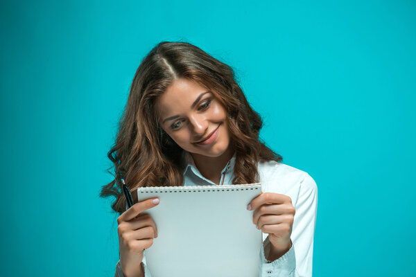 The smiling young business woman with pen and tablet for notes on blue background