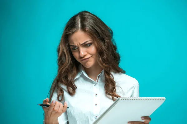 Невдоволена молода бізнес-леді з ручкою і планшетом для нотаток на синьому фоні — стокове фото