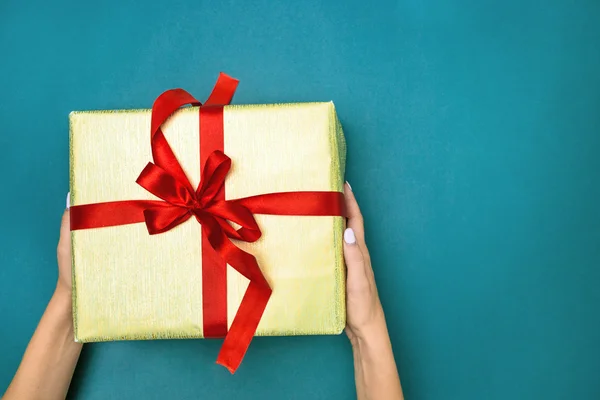 Manos femeninas sosteniendo regalo sobre fondo azul — Foto de Stock